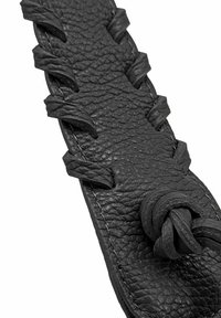 Bracelet en cuir noir avec une surface texturée, détails tressés le long des bords et accents noués, cousu avec un fil blanc.