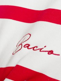 Tessuto bianco con audaci strisce orizzontali rosse e testo ricamato in rosso "Bacio" posizionato diagonalmente sul materiale.