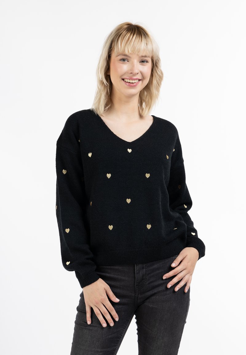 Pulover negru cu decolteu în V, având modele de inimi aurii. Textură moale, tricotată; mâneci lungi; croi lejer. Poartă cu blugi închisi la culoare.