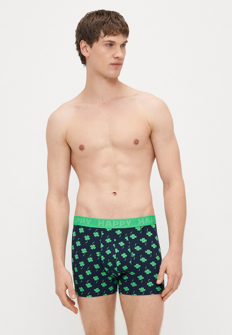 Μπόξερ σλιπ σε ναυτικό μπλε με πράσινο μοτίβο τριφυλλιού. Η ελαστική μέση έχει το κείμενο "HAPPY" με έντονα γράμματα. Μαλακό, ελαστικό ύφασμα.