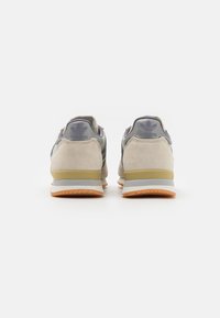 Beige och grå mockaskor med nätpaneler, gummiyttersula och lila accenter, med adidas-logotyp på hälen.