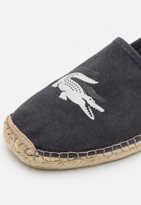 Espadrille en toile bleu marine foncé avec un design sans lacets. Dotée d'un logo crocodile blanc et d'une semelle en jute tissée. Tissu texturé et accents cousus.