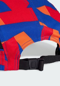 A sapka színes geometrikus mintával rendelkezik, piros, kék és narancs minták találhatóak rajta. Hátsó állítható fekete pántja műanyag csat segítségével állítható.