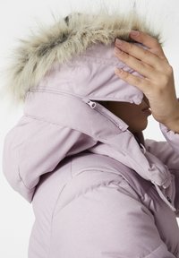 Světle fialová péřová bunda s kapucí podšitou umělou kožešinou. Má zapínání na zip a knoflík, texturovanou tkaninu a měkký vzhled.