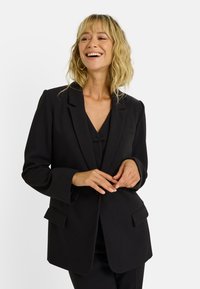Blazer noir avec revers crantés, manches longues et poches à rabat. Tissu lisse avec une coupe ajustée et un design minimaliste.