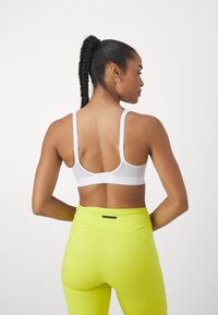 Sutien sport alb cu bretele ajustabile, închidere prin clips, combinat cu colanți neon galbeni cu talie înaltă. Textură netedă, design minimalist.