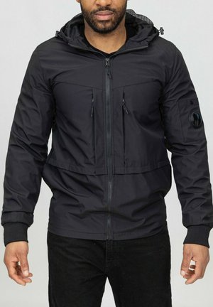 Veste à capuche noire avec fermeture éclair sur le devant, poches latérales et une poche sur une manche. Fabriquée en matériau lisse et résistant à l'eau avec une finition légèrement texturée.