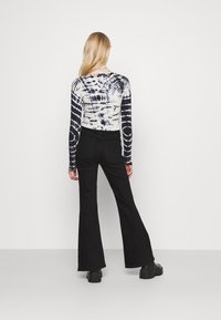 Długi rękaw w tye-dye w czarno-białym kolorze, zestawiony z wysokim stanem czarnych spodni dzwonowych. Gładki materiał o dopasowanym kroju.