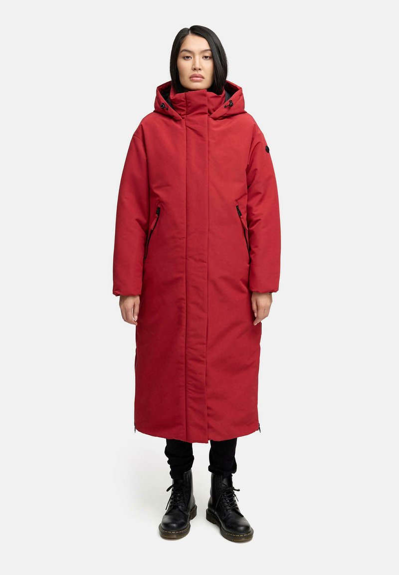 Rød lang frakke med hætte, der har et polstret design, frontlynlås og sidelommer. Båret over sorte bukser og støvler, ensfarvet baggrund.