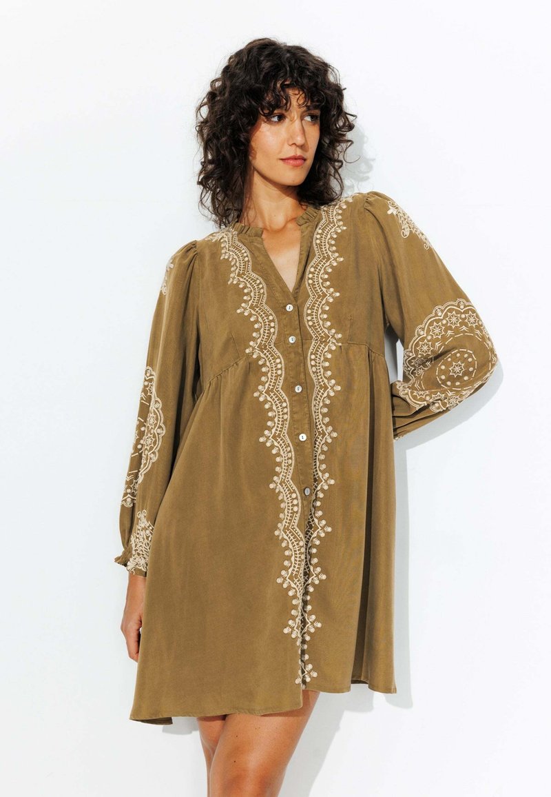 Robe verte olive, longueur genou, avec une broderie blanche complexe le long de l'avant et des manches, dotée d'un boutonnière et d'une coupe décontractée.