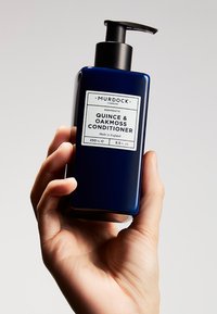 Bouteille en plastique bleu foncé de conditionneur Quince & Oakmoss avec un bouchon-pompe noir. L'étiquette présente du texte incluant le nom de la marque et les détails du produit.