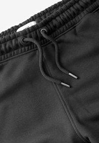 Zwarte trainingsbroek met een elastische tailleband en trekkoord. Voorzien van metalen tips aan het trekkoord en zachte, gestructureerde stof.