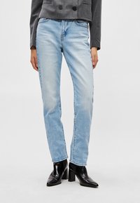 Világoskék egyenes szárú farmer, kopott hatású mosással, ötlukú zsebes kialakítással és kontrasztos varrással, fekete sarkú csizmával párosítva.