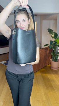 Sac à main en cuir noir avec une finition lisse, une anse arrondie sur le dessus et un tirant de fermeture éclair en argent. Le sac présente des coutures discrètes et un design minimaliste.