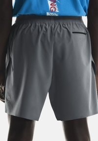 Des shorts de sport gris présentent une texture légère et douce, avec une taille élastique, des poches latérales et une petite poche arrière zippée.