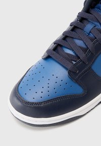 Sapatilha de couro azul com sobreposição azul-marinho, design de biqueira perfurada e atacadores azul-marinho. Apresenta uma sola de borracha branca.