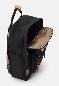Zaino in tessuto nero con interni color sabbia, spallacci regolabili e dettagli in pelle. Presenta una tasca esterna e un'apertura con zip.