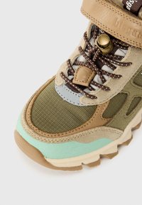 Basket verte et beige avec une tige texturée, un col rembourré, des accents menthe contrastants et un système de laçage proéminent avec un système de boucle.