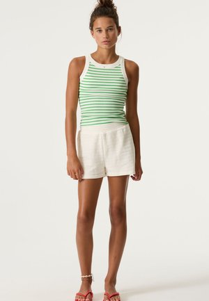 Groen-wit gestreept tanktop met een geribbelde textuur, gecombineerd met witte geperforeerde korte broek. Model staat met handen langs het lichaam, draagt roze sandalen.