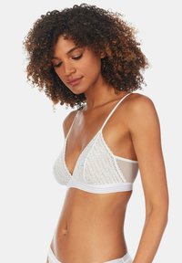Biały biustonosz braletka z przezroczystą siateczką i fakturowanymi koronkowymi miseczkami, z wąskimi ramiączkami i solidnym pasem. Falbany dodają szczegółu.