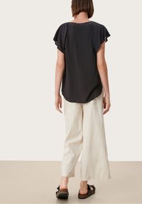 Blusa nera a maniche corte con scollatura rotonda, abbinata a pantaloni larghi color crema e scarpe basse nere con dettagli intrecciati.