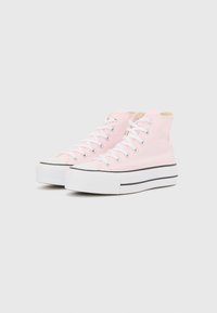 Rosa hightop sneakers i canvas med vita snören, en tjock vit sula och svarta accentsträck längs botten.