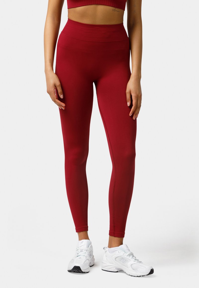 Red high-waisted leggings made of stretchy fabric, featuring a smooth texture and fitted design, paired with white athletic shoes.