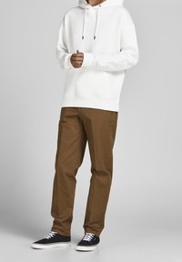 Felpa bianca con cappuccio abbinata a pantaloni marroni e sneaker nere con lacci bianchi. La felpa ha una vestibilità comoda e coulisse.