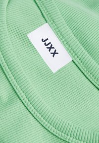 T-shirt verde canelado com decote redondo e uma etiqueta rotulada "JJXX" costurada. O tecido tem uma textura suave com riscas subtis.