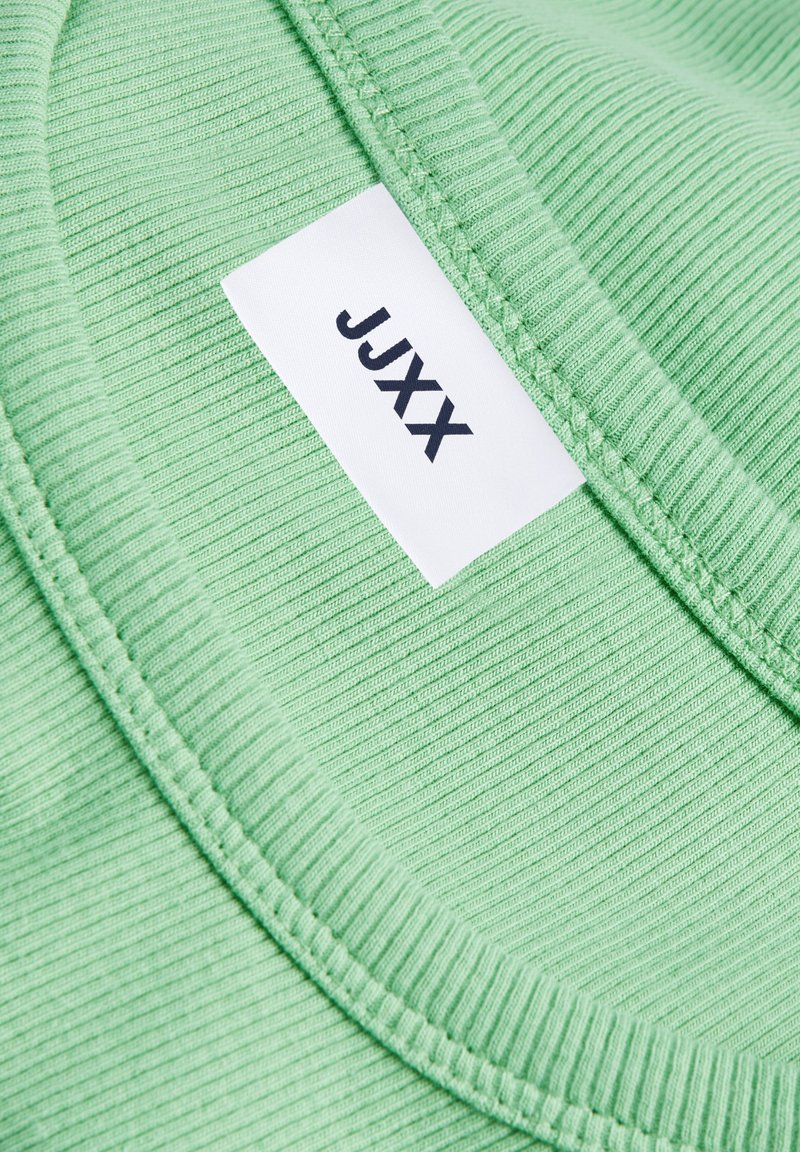 Zielona, prążkowana koszulka z okrągłym dekoltem i metką z napisem "JJXX" wszytą. Materiał ma miękką teksturę z delikatnymi wypustkami.