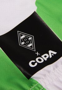 Voetbalshirt met een wit lichaam en groene accenten. Zwarte label toont logo met "B" en "COPA" in witte lettertype. Zachte, gestructureerde stof.