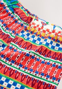 Tissu coloré à motifs comprenant des dessins rouges, bleus, jaunes et verts avec des formes géométriques et abstraites. Détail de ceinture élastique visible.