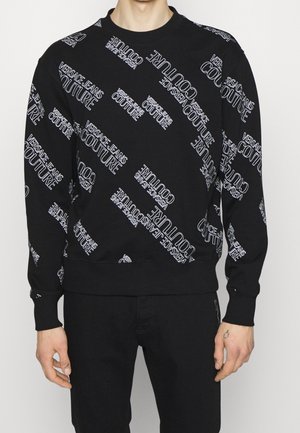 Czarna bluza z długim rękawem z białym napisem "Versace Jeans Couture" drukowanym na ukos na przodzie i rękawach.