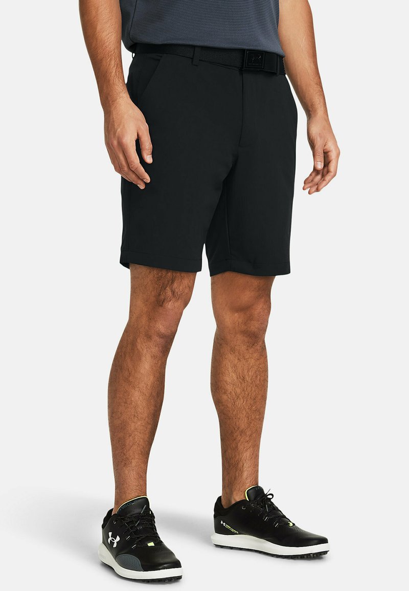 Pantaloni scurți negri cu o croială ajustată, dintr-un material ușor. Au buzunare laterale și o textură netedă, asociați cu încălțăminte sport neagră.