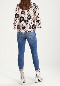 Blusa floreale con fiori neri su uno sfondo rosa, abbinata a jeans skinny blu e stivali alla caviglia argentati. Presenta maniche a campana.