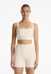 Beige sports bra with square neckline and wide straps, featuring perforated detailing. Paired with matching high-waisted shorts.