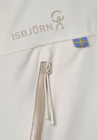 Hvid jakke med en tekstureret overflade, der har en lynlås og et lille blå og gult flagdetalje. Mærket er diskret præsenteret.