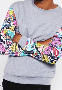 Sudadera gris de manga larga con impresiones gráficas coloridas de alimentos, patrones y símbolos. Tejido suave, diseño casual.