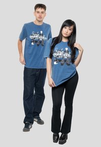 Blue, cotton t-shirts with a graphic print featuring cartoon characters. The male model wears loose jeans, while the female model has fitted pants.