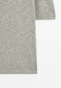 Gros plan sur un tissu tricoté côtelé gris clair avec un bord de manche rectangulaire sur fond blanc.