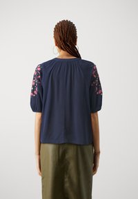 Marinblus med korta puffärmar, med blomstermönster på axlarna, texturerad tyg, rund halsringning och ledig passform.