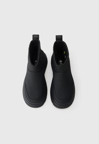 Fekete, slip-on téli csizma pár húzófülekkel és vastag talpakkal, felülről nézve, fehér háttér előtt.