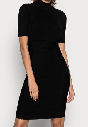 Robe en tricot noir côtelé avec un col haut et des manches courtes. Silhouette ajustée avec des détails texturés au niveau de la taille et de la jupe.
