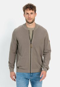 Khaki gebreide cardigan met ritssluiting, textuurstof, geribde manchetten en een staande kraag. Voorzien van zijzakken en een rits met een decoratieve trekker.