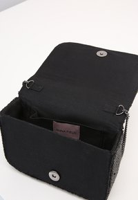 Černá látková kabelka s klopou na zapínání, vybavená stříbrným patentním knoflíkem a řetízkovým popruhem. Uvnitř je kapsa a značená etiketa.