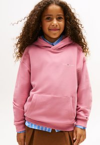 Sweatshirt rosa com capuz e bolso frontal, feito de material suave. Apresenta um pequeno logotipo e punhos canelados, sobreposto a uma camisa azul com riscas.