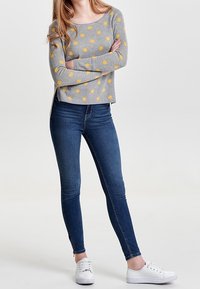 Pull gris à pois jaunes, texture côtelée, encolure dégagée, associé à un jean skinny bleu foncé et des baskets blanches.