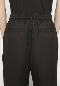 Zwarte, lichtgewicht broeken met een elastische tailleband, voorzien van een gladde textuur en twee achterzakken. Eenvoudig, recht model.