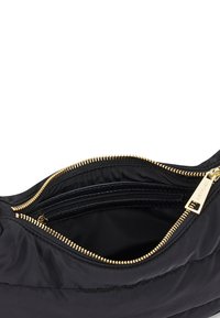 Sac à main matelassé noir avec des accessoires en or, doté d'une fermeture zippée sur le dessus et d'une poche intérieure. Texture douce et forme structurée.