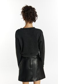 Zwarte geribbelde trui met een brede halslijn, lange mouwen en een cropped pasvorm, gecombineerd met een glimmende zwarte leren minirok.